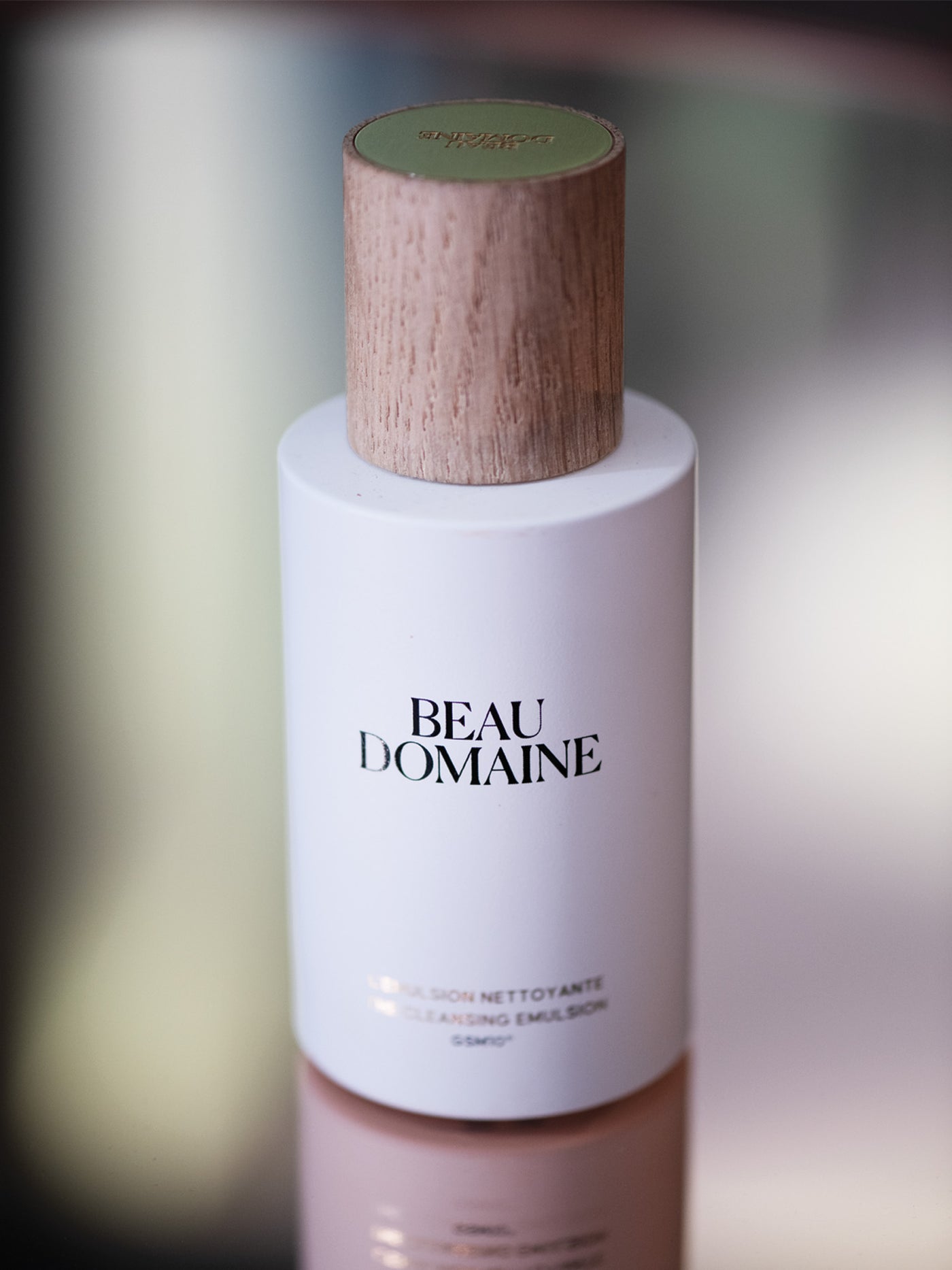 Beau Domaine ādas kopšanas pudelīte ar koka vāciņu uz izplūduša fona.